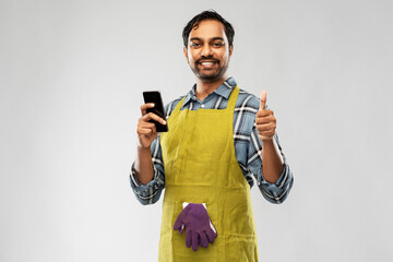 Poster - gardening, farming and technology concept - happy smiling indian male gardener or farmer in apron using smartphone showing thumbs up over grey background