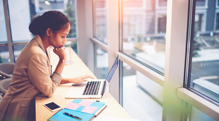 Portrait of concentrated afroamerican coach checking coursework of students about business concept of successful startup sitting at table working via laptop computer connected to wireless internet