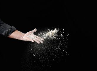 Wall Mural - baker's male hand throws up a handful of white wheat flour on a black background