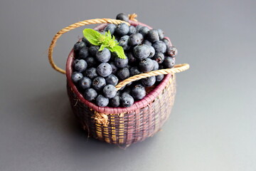 Wall Mural - Blueberries with green leaves in a wicker basket on a gray background. Blueberry antioxidant. Healthy food and nutrition concept