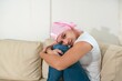© Hector Pertuz - A young woman with cancer wears a pink headscarf, sitting on the couch in her house, smiling. Woman with cancer sitting after chemotherapy sessions