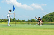 © freebird7977 - Golfer man and friend playing golf aiming shot for putting ball on the hole with club on green course.