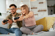 © JustLife - Husband and wife playing video game with joysticks in living room. Loving couple are playing video games at home..