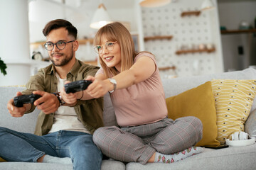 Wall Mural - Husband and wife playing video game with joysticks in living room. Loving couple are playing video games at home..