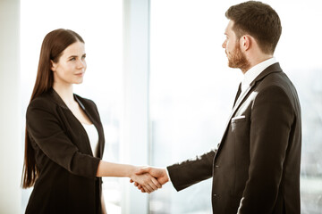 Successful business concept. Young businesswoman and businessman shake hands after signing partnership cooperation contract in office. Two managers man and woman teamwork indoors.