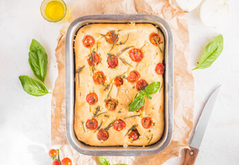 Traditional italian focaccia bread with tomatoes and rosemary in mental baking tray . On the beige brown paper and white concrete background.