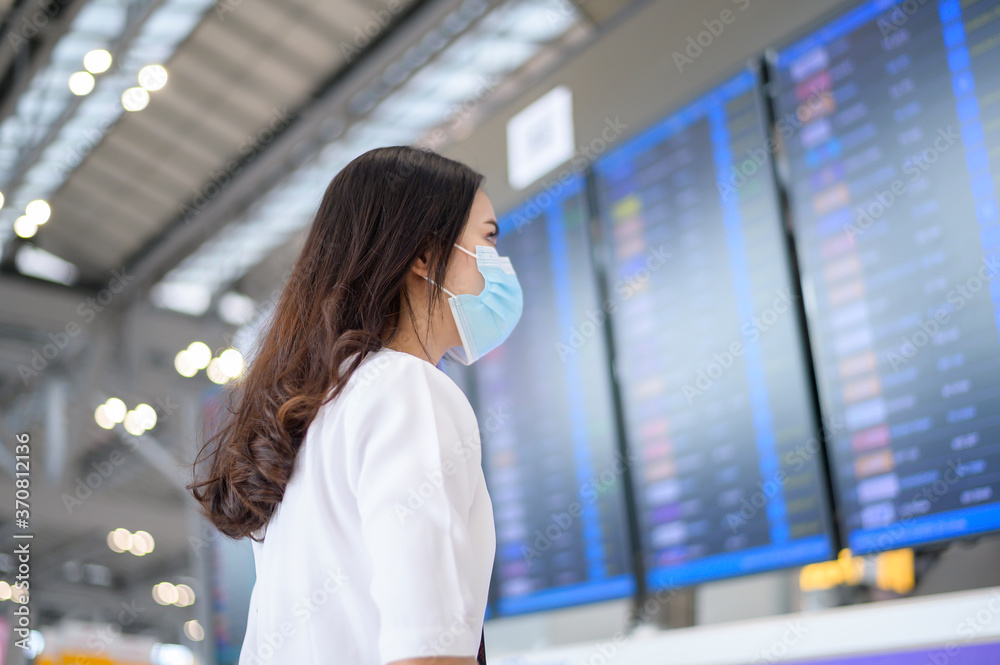 A traveller woman is wearing protective mask in International airport, travel under Covid-19 pandemic, safety travels, social distancing protocol, New normal travel concept - obrazy, fototapety, plakaty 