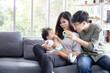 © charnsitr - Asian LGBTQ Couple Play with Their Adopted Baby on the Sofa in the Living Room