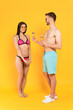 © LIGHTFIELD STUDIOS - man in sunglasses holding ice cream cones near happy girl in swimsuit on yellow