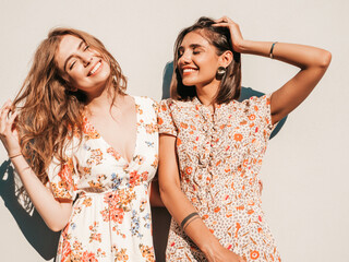 Wall Mural - Two young beautiful smiling hipster girls in trendy summer sundress.Sexy carefree women posing near wall on the street background. Positive models having fun and hugging