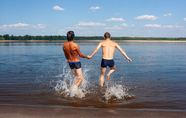 Two men run into the water and hold hands