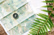 © Alberto Menendez/ADDICTIVE STOCK - Top view of paper map and modern compass placed on rock with fern leaf in forest