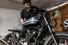 Low Angle Of Brutal Male Mechanic Standing In Shabby Workshop And Repairing Motorbike