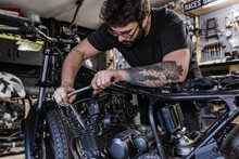 Side View Of Crop Male Mechanic Using Socket Wrench And Fixing Motorbike In Workshop