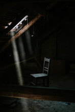 Creepy Scene Of A Wooden Chair Placed Next To A Skylight Inside An Abandoned Attic