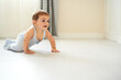 © Gabriel Trujillo/ADDICTIVE STOCK - Side view of adorable little baby in gray bodysuit smiling while crawling on floor in cozy room at home