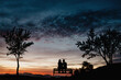 © Gustavo Pozo/ADDICTIVE STOCK - Back view silhouettes of affectionate couple enjoying romantic date while sitting on bench against cloudy sunset sky in summer evening