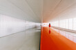 © Javier Bravo/ADDICTIVE STOCK - Back view of unrecognizable female standing on shiny orange floor of passage in modern building
