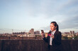 © Juan Alberto Ruiz/ADDICTIVE STOCK - Side view of serious young Asian businesswoman in formal wear holding credit card and smartphone with bank customer service while standing on rooftop of city building