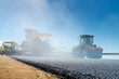 © Kavi Sanchez/ADDICTIVE STOCK - Ground level of employees in uniforms standing near road roller and asphalt spreading machine on background of blue sky