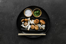 Top View Of Bowl With Various Raw Mushrooms Placed On Black Table With Chopsticks In Kitchen Near Salt And Parsley