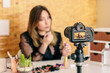 © Pedro Talens/ADDICTIVE STOCK - Charming female influencer in elegant wear applying lipstick while looking at camera making a tutorial recording video on professional camera