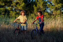 Ten-year-old Boy And Girl Riding Their Bicycles Through The Countryside, With A Case A Backpack And Some Glasses