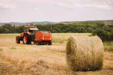Dried Hay Roll And Modern Tractor Placed On Agricultural Field In Mountainous Area In Summer