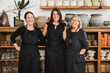 © Raquel Arocena/ADDICTIVE STOCK - Positive professional female florists in black aprons smiling and looking at camera friendly while standing against shelves with various flower pots in stylish floristry shop