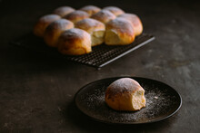 From Above Of Delicious Fresh Round Buns With Soft Texture And Golden Surface Decorated With Powdered Sugar On Cooling Rack And Table On Black Blurred Background