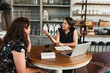 © Raquel Arocena/ADDICTIVE STOCK - Side view of female owner of stylish floristry salon discussing details of order with customer while sitting together at table with laptop