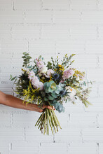 Crop Anonymous Female Holding Beautiful Blooming Bouquet Of Various Fresh Flowers And Decorative Plants Against White Brick Wall