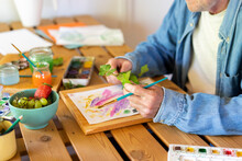 Senior Man Holding Leaves While Painting On Table At Home
