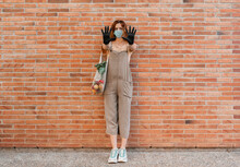 Woman Wearing Mask And Gloves Showing Hands While Standing On Footpath Against Brick Wall