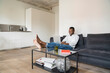 © Westend61 - Portrait of smiling man sitting on couch in modern apartment using laptop