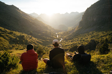 Group of young men sitting on the grass watching the sunset on top of a valley in Pyrenees