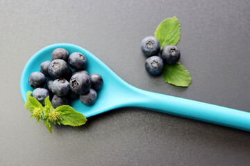 Wall Mural - Fresh blueberries with green leaves in a blue bamboo spoon on a gray background. Blueberry antioxidant. Healthy food and nutrition concept