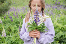 Portrait Of Girl With Eyes Closed Standing In Front Of Flower Field Holding Bunch Of Lupines