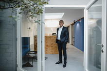Senior businessman standing in open office door with hands in pockets