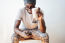 Smiling Man Text Messaging While Holding Coffee Cup And Sitting Against White Background