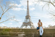 Woman using smart phone while standing on bridge with Eiffel Tower in background, Paris, France