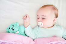 Portrait Of Sleeping Baby Girl With Pacifier And Cuddly Toy