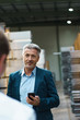 © Westend61 - Businessman holding mobile phone looking at colleague in a factory