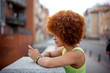 © Westend61 - Mid adult woman with afro hair using smart phone while standing by retaining wall