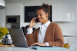 © Westend61 - Smiling businesswoman on the phone sitting in kitchen working on laptop