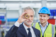 © Westend61 - Confident male manager looking through brass object with supervisor in background at factory