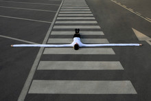 Woman With Artificial Long Hands Lying With Arms Outstretched On Zebra Crossing