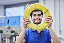 Confident Male Worker Looking Through Rolled Up Cables In Factory