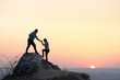 © bilanol - Man and woman hikers helping each other to climb stone at sunset in mountains. Couple climbing on high rock in evening nature. Tourism, traveling and healthy lifestyle concept.