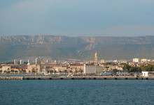 View Of Split, Croatia Town From A Car Ferry Approaching For Very Far. Church Belltower Seen Rising Above The Old Buildings, Mountains And Sky In The Distance